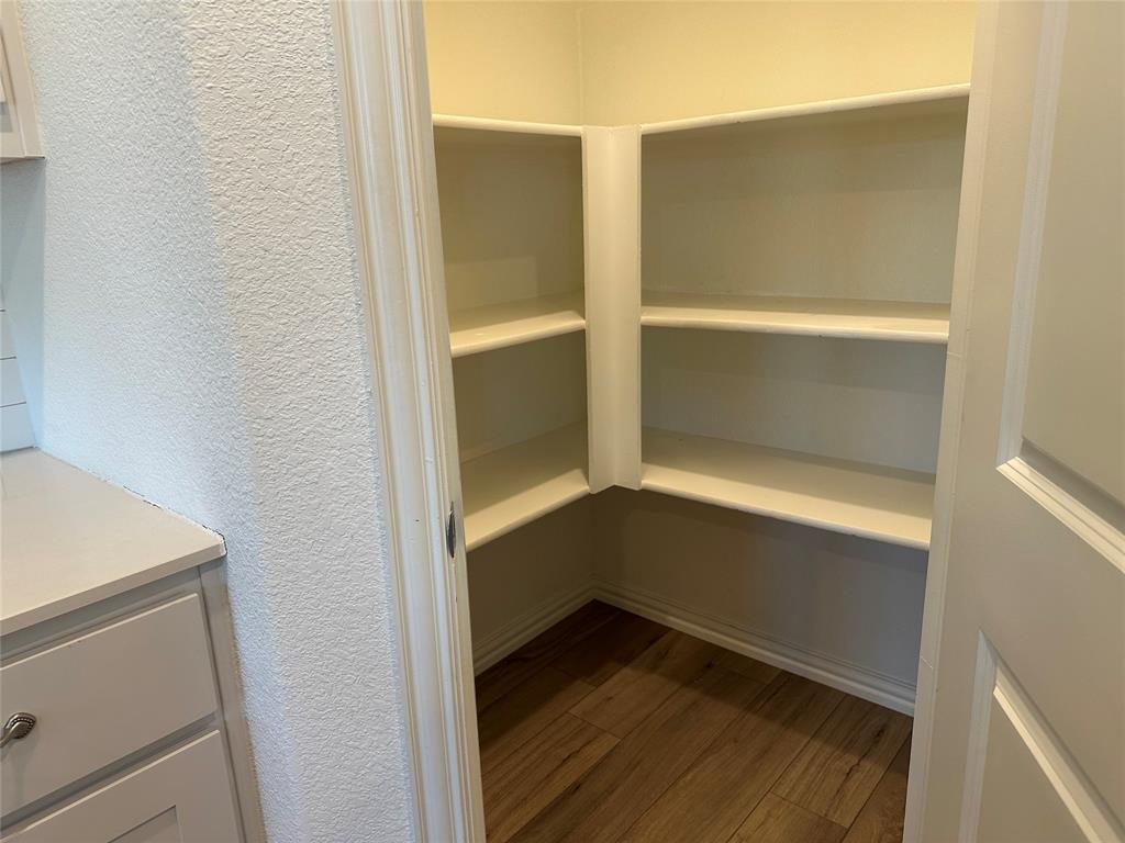 Walk-in storage space featuring wood-finish flooring and multiple tiers of built-in shelving