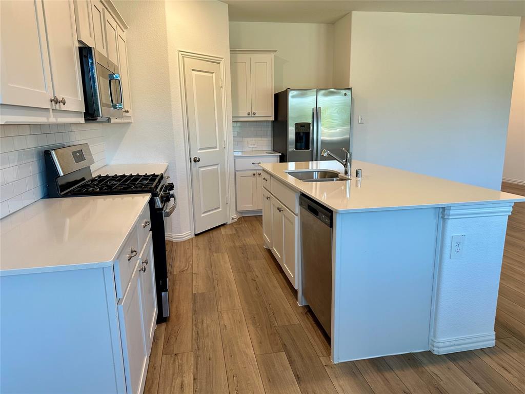 Kitchen featuring white cabinetry, solid-surface countertops, subway tile backsplash, stainless steel appliances, and wood-finish flooring