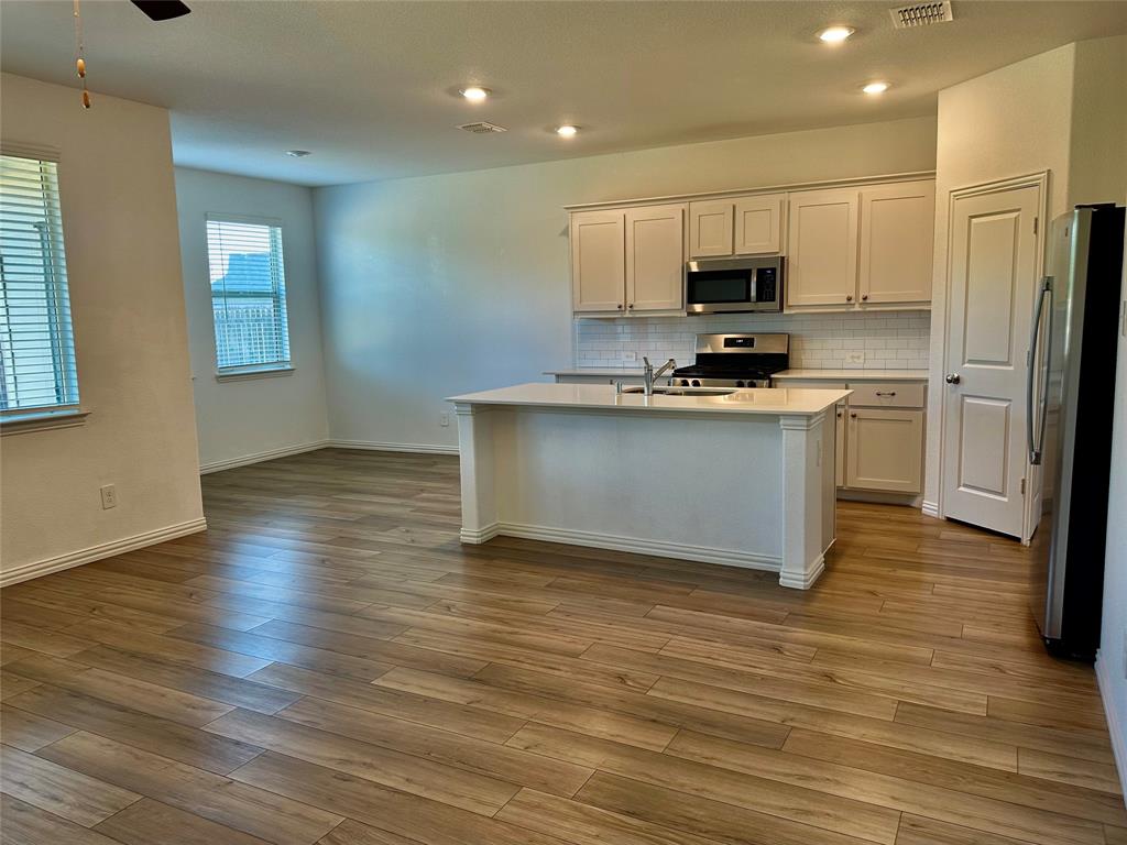 Kitchen featuring wood-finish flooring, white cabinetry, a center island with a light-toned countertop, subway tile backsplash, and recessed lighting