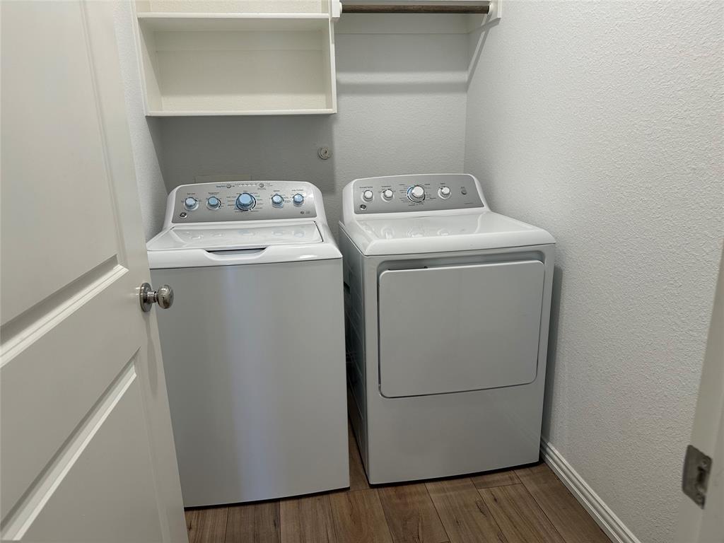 Laundry area featuring wood-finish flooring, white built-in shelving, and a wall-mounted hanging rod