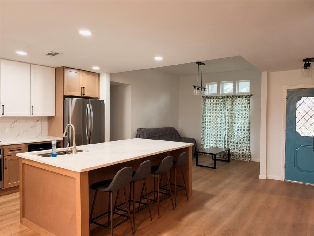 Kitchen featuring a central island with a solid-surface countertop, two-tone cabinetry, stainless steel refrigerator, recessed lighting, and wood-finish flooring