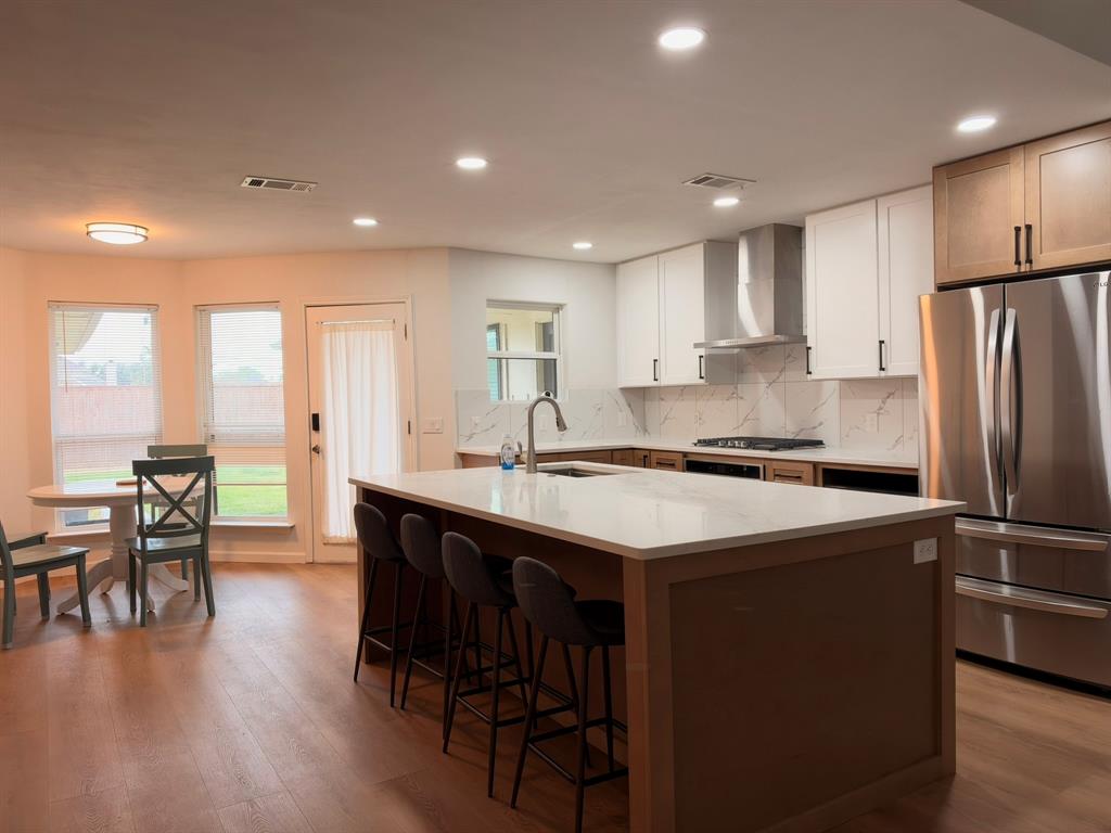 Kitchen featuring a center island with a stone-finish countertop, stainless steel refrigerator, white shaker-style cabinetry, recessed lighting, and stone-finish backsplash