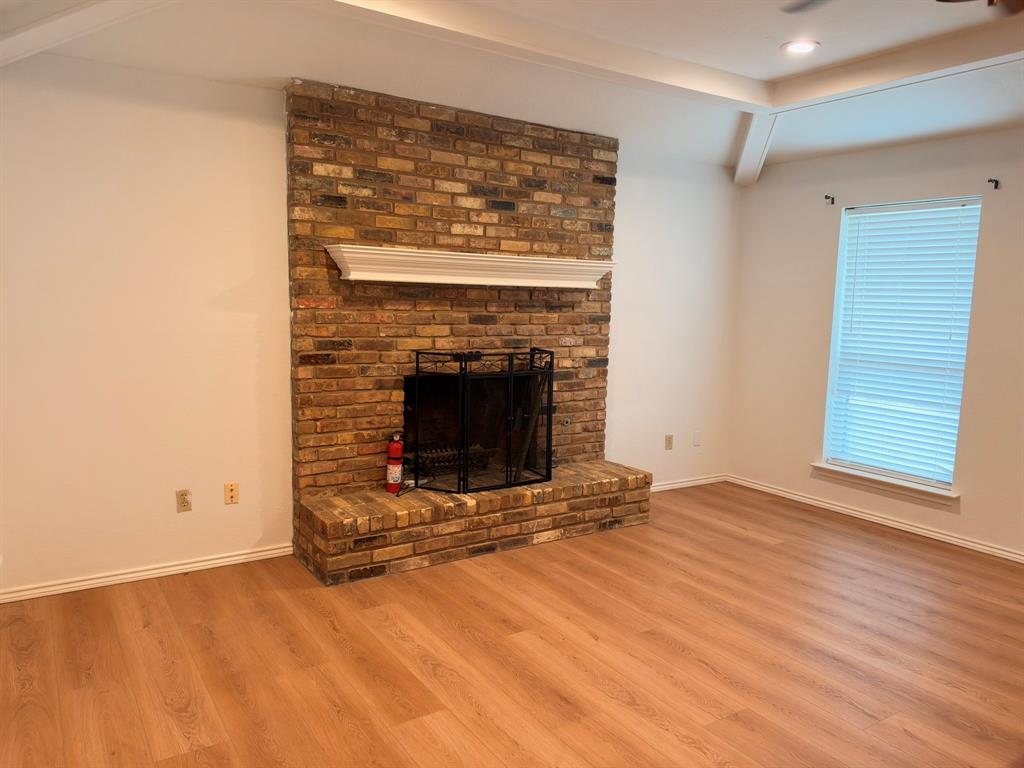 Floor-to-ceiling brick fireplace with an elevated hearth and white mantle, featuring wood-finish flooring and a tray ceiling Floor-to-ceiling brick fireplace with an elevated hearth and white mantle, featuring wood-finish flooring and a tray ceiling