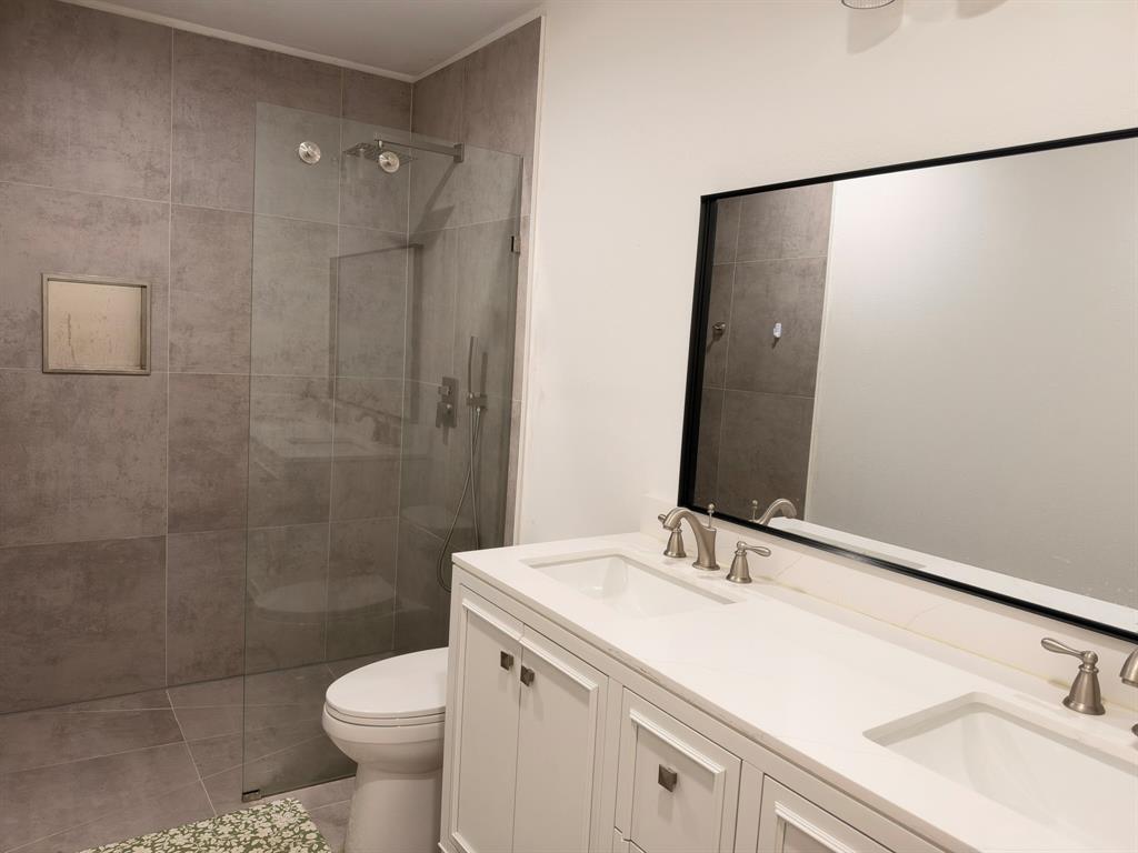 Dual-sink vanity with white cabinetry and countertop, large rectangular mirror with black frame, walk-in shower with floor-to-ceiling tile, and integrated wall niche Dual-sink vanity with white cabinetry and countertop, large rectangular mirror with black frame, walk-in shower with floor-to-ceiling tile, and integrated wall niche