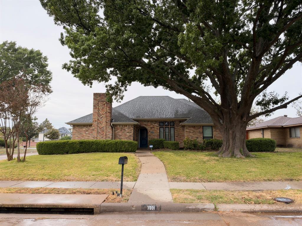Single-story brick exterior featuring a prominent chimney with herringbone masonry detailing, hipped roofline, and mature landscaping Single-story brick exterior featuring a prominent chimney with herringbone masonry detailing, hipped roofline, and mature landscaping