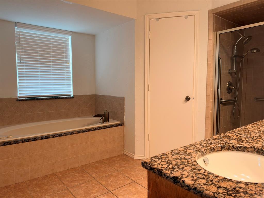 Built-in soaking tub with a tiled surround, stone-finish countertop vanity, glass-enclosed shower with a multi-function showerhead, and tile flooring
