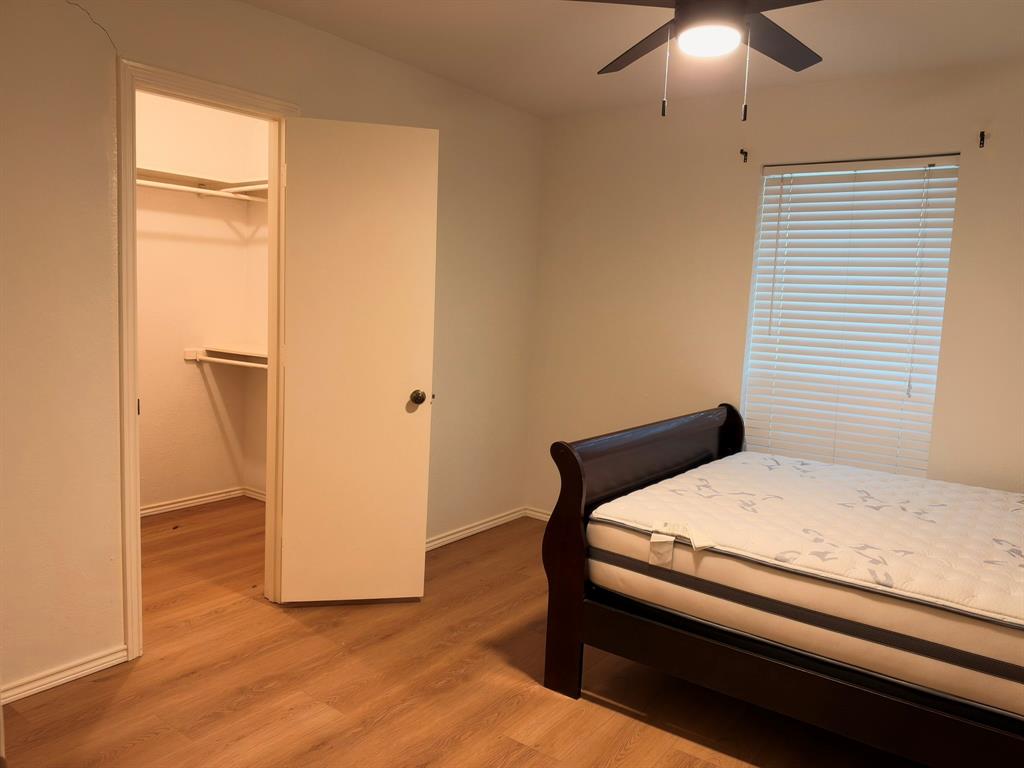 Wood-finish flooring, closet with built-in shelving, window with horizontal blinds, and ceiling fan with integrated lighting