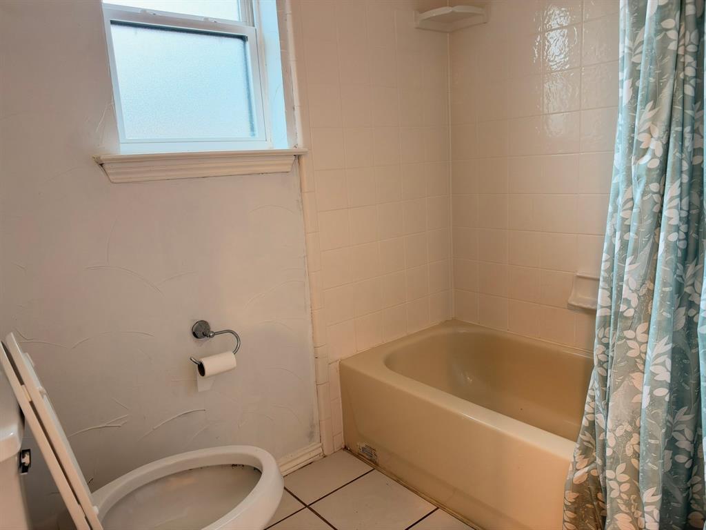Bathroom featuring a porcelain bathtub, square-tile wall surround, frosted glass window, and ceramic floor tiling