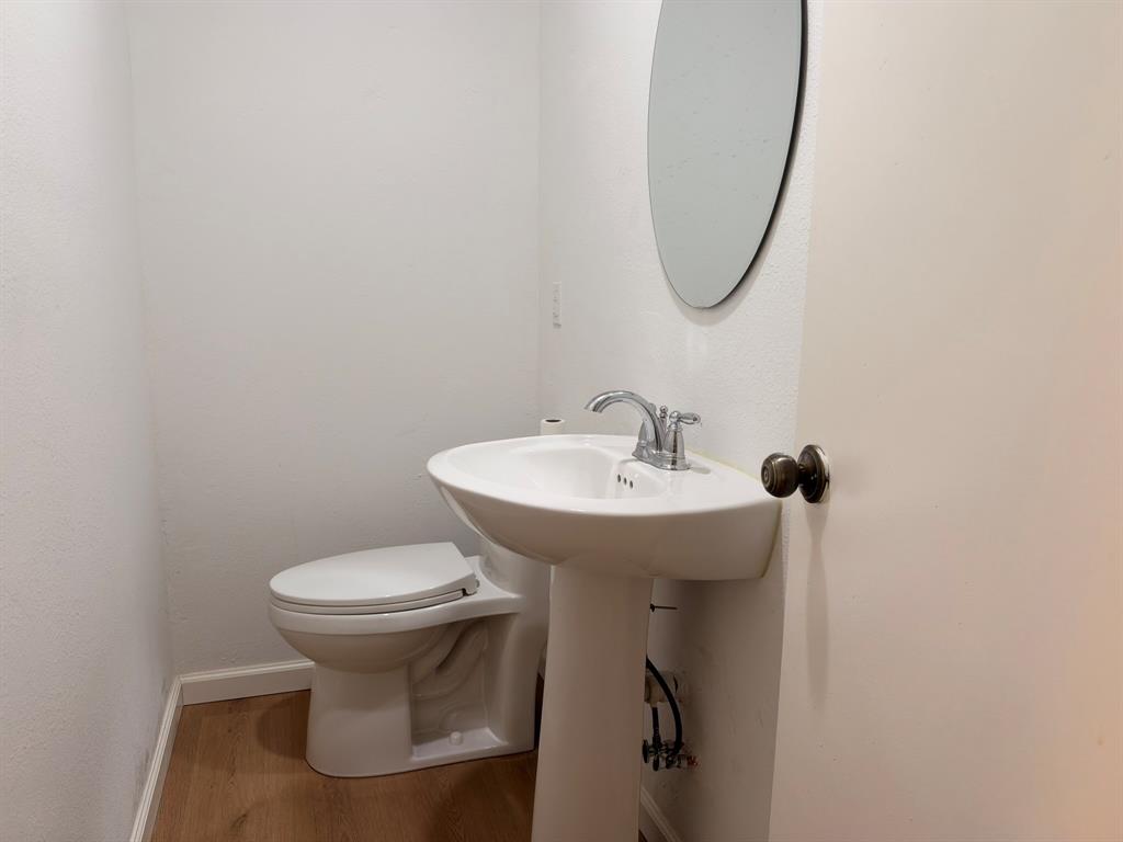White pedestal sink with chrome faucet, porcelain toilet, oval wall-mounted mirror, and wood-finish flooring
