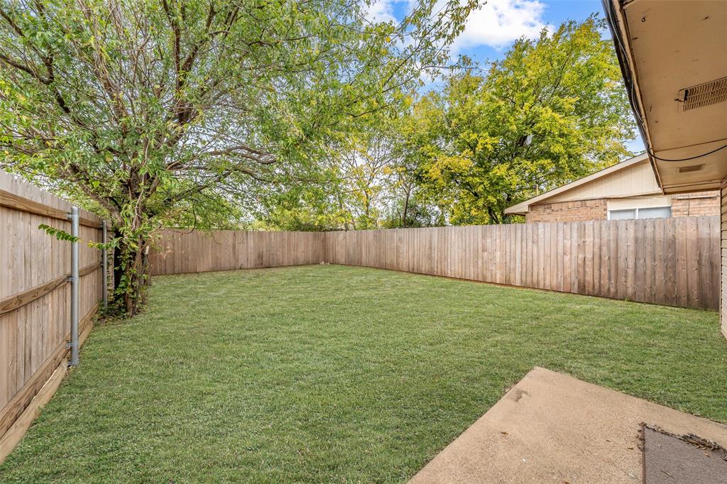 1128 Backyard featuring a grass lawn, wood perimeter fencing, concrete patio, and mature trees