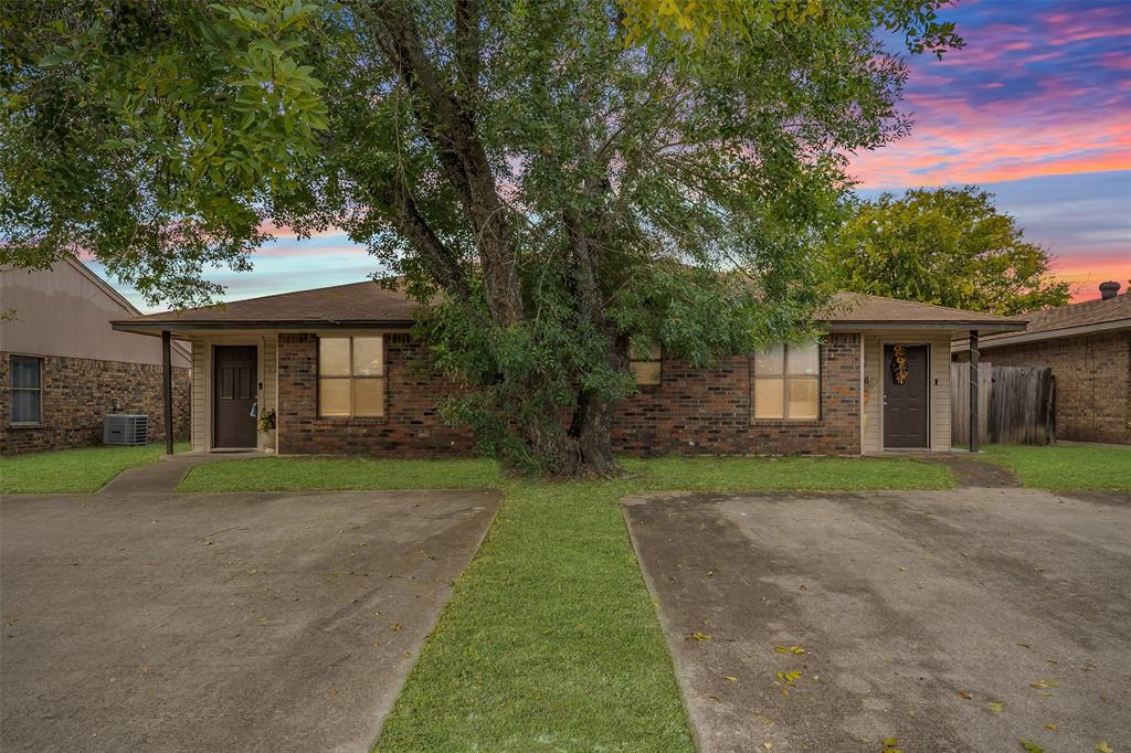 Single-story brick exterior featuring a low-slope roof, dual entry doors, paved surface parking, and mature trees Single-story brick exterior featuring a low-slope roof, dual entry doors, paved surface parking, and mature trees