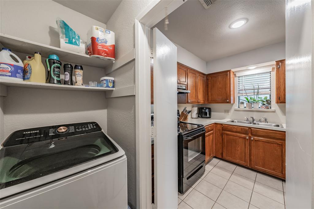 1128 Laundry area featuring built-in shelving, tile flooring, and wood cabinetry, including a stainless steel sink and integrated range