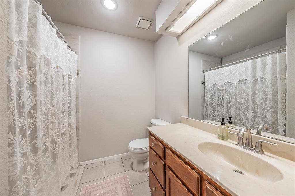 1128 Bathroom featuring a wood-finish vanity with a stone-composite countertop, integrated oval basin, recessed lighting, and a large-format mirror