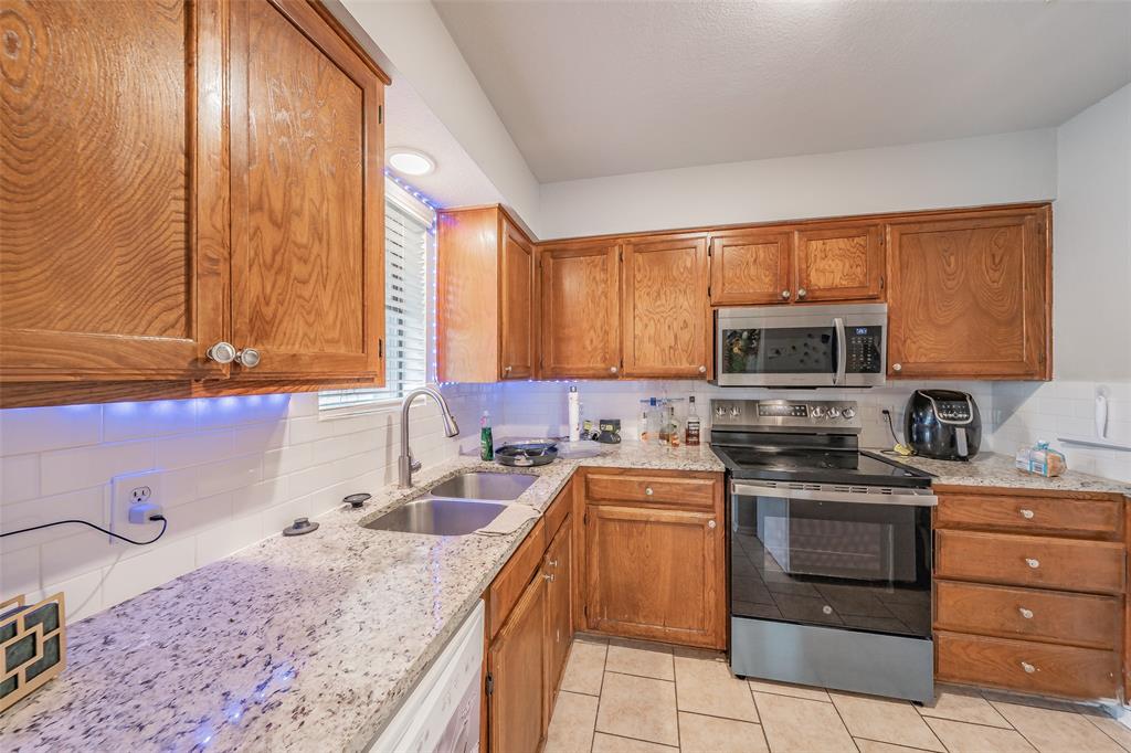 1126 Kitchen featuring wooden cabinetry, stone-finish countertops, subway tile backsplash, stainless steel appliances, and tile flooring