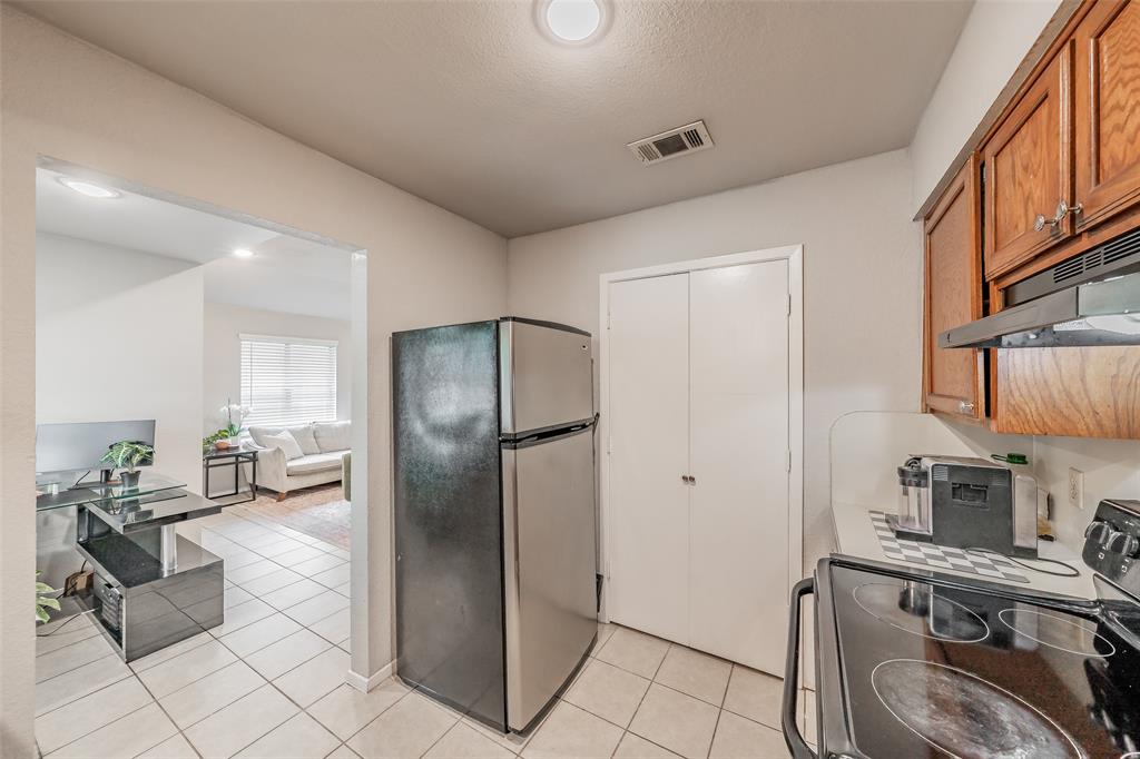 1128 Kitchen featuring wood cabinetry, stainless steel refrigerator, black electric range with an integrated hood, and tile flooring