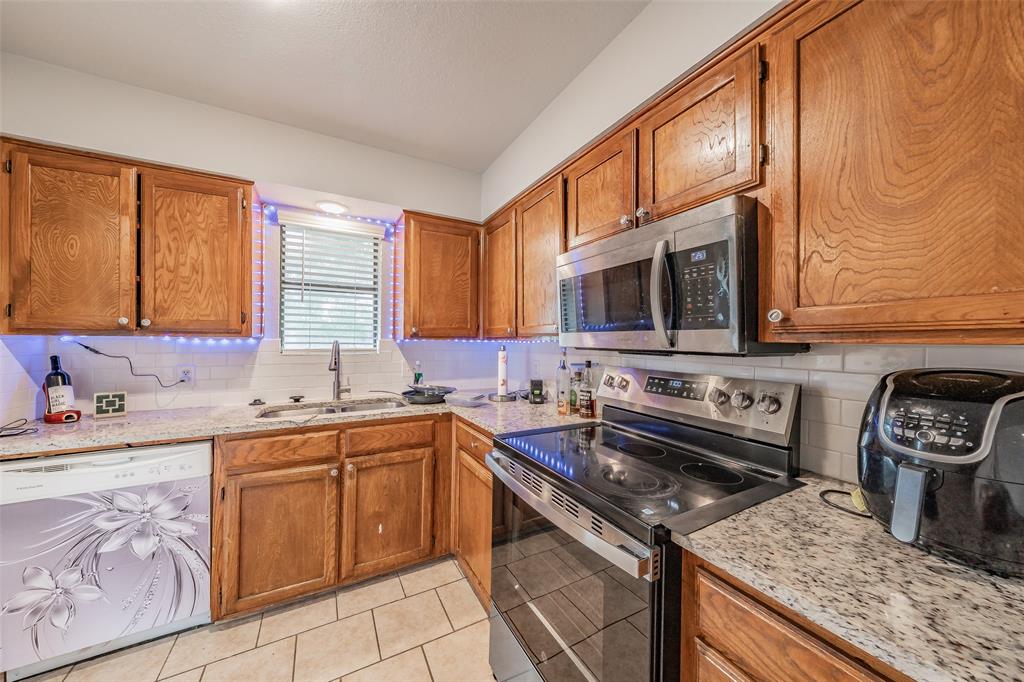 1126 Kitchen featuring wood cabinetry, stone-finish countertops, subway tile backsplash, stainless steel microwave, and tile flooring