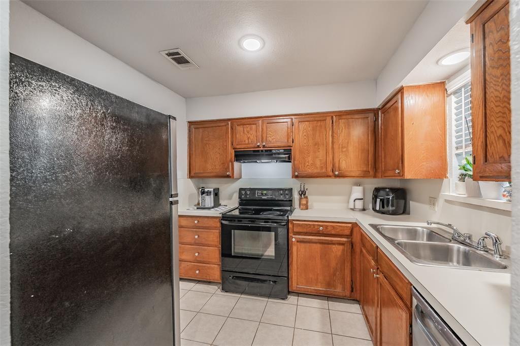 1128 Kitchen featuring stained wood cabinetry, solid-surface countertops, dual-basin stainless steel sink, black built-in oven range, and tile flooring