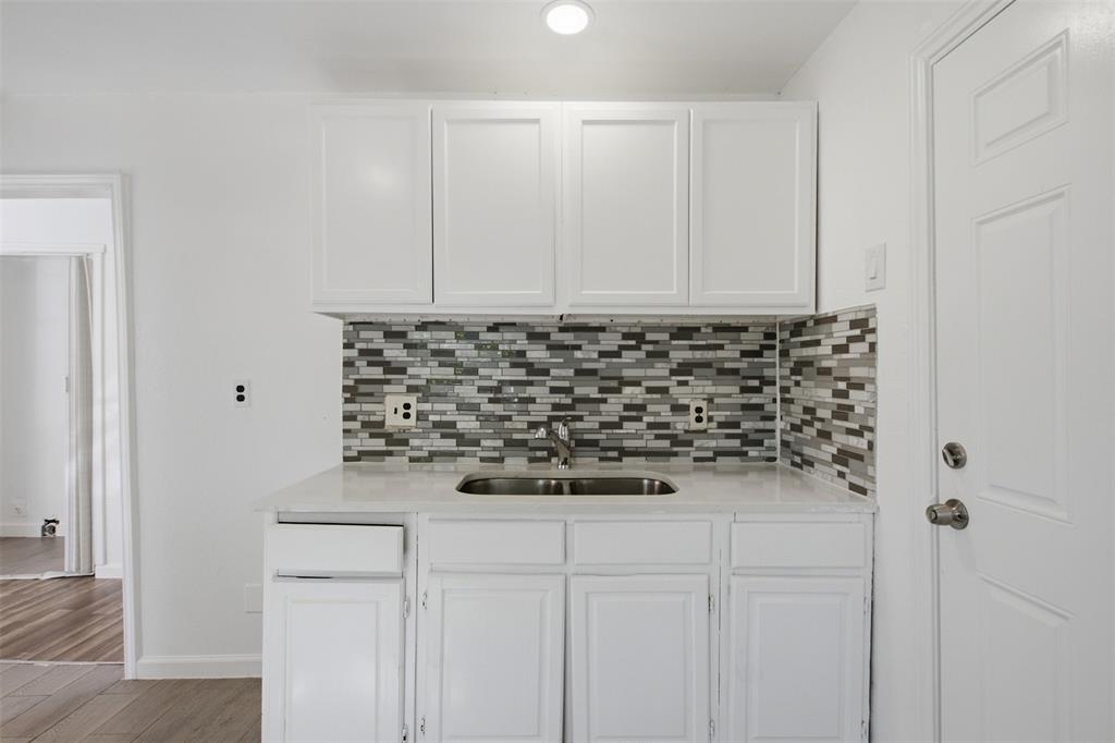 Kitchenette featuring white cabinetry, a neutral solid-surface countertop, an integrated stainless steel sink with a metallic faucet, and a multi-toned linear tile backsplash