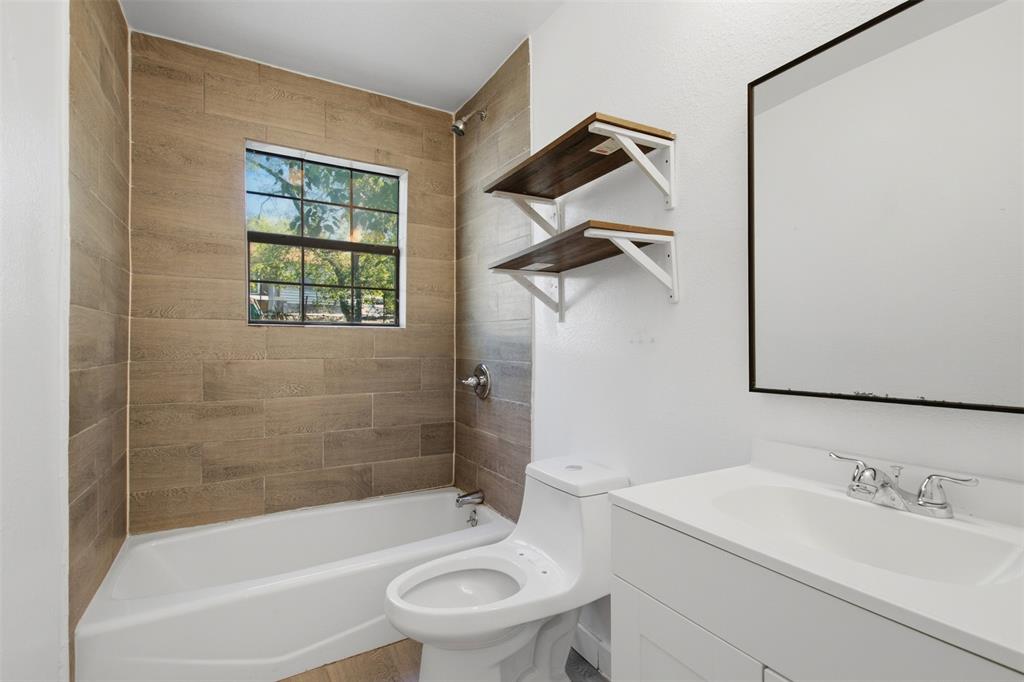 Bathroom featuring wood-finish tile shower surround, built-in wall shelving, white vanity with integrated sink, and black-framed mirror