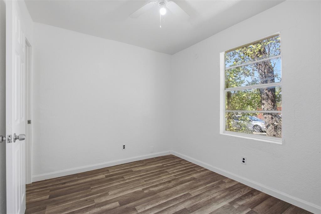 Neutral interior room featuring wood-finish flooring, crisp white walls, a multi-pane window, and a ceiling-mounted light fixture