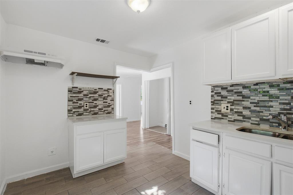 Kitchen featuring white shaker-style cabinetry, multi-toned horizontal mosaic tile backsplash, solid-surface countertops, wood-finish tile flooring, and integrated metal range hood