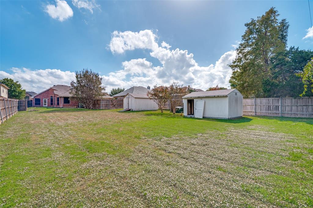 Expansive backyard featuring a large grass lawn, perimeter wood fencing, and two detached storage structures