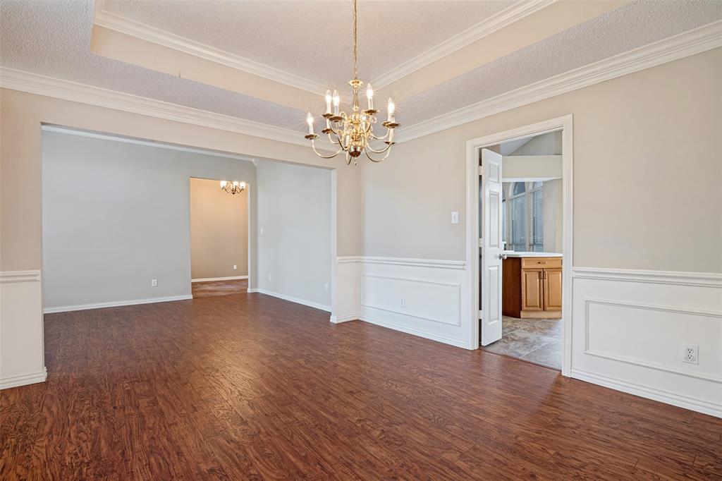 Formal dining area featuring wood-finish flooring, recessed tray ceiling, decorative wainscoting, and a multi-arm brass chandelier Formal dining area featuring wood-finish flooring, recessed tray ceiling, decorative wainscoting, and a multi-arm brass chandelier