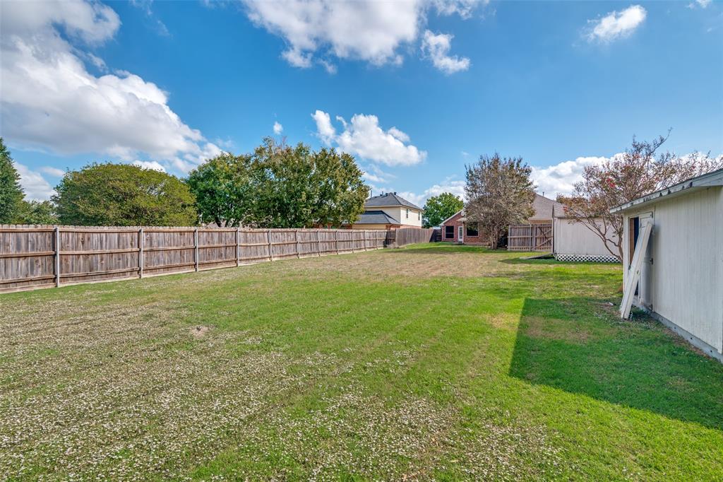 Expansive backyard featuring a natural grass lawn, full-perimeter wood fencing, and a detached storage structure