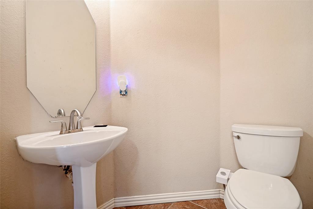 Pedestal sink with a dual-handle faucet, wall-mounted octagonal mirror, and ceramic toilet