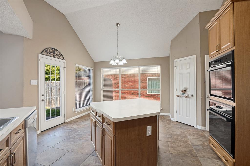 Vaulted ceiling, center island with solid surface countertop, tile flooring, integrated double wall oven, and a multi-light chandelier