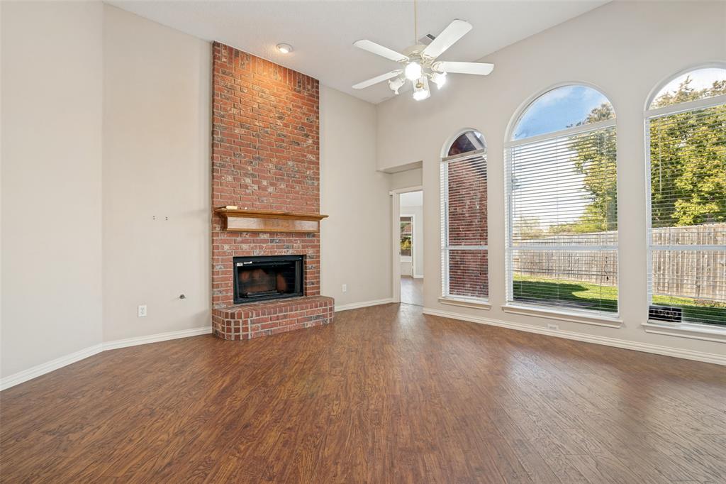 Floor-to-ceiling red brick fireplace with a wood mantel, high vaulted ceilings, wood-finish flooring, and arched windows