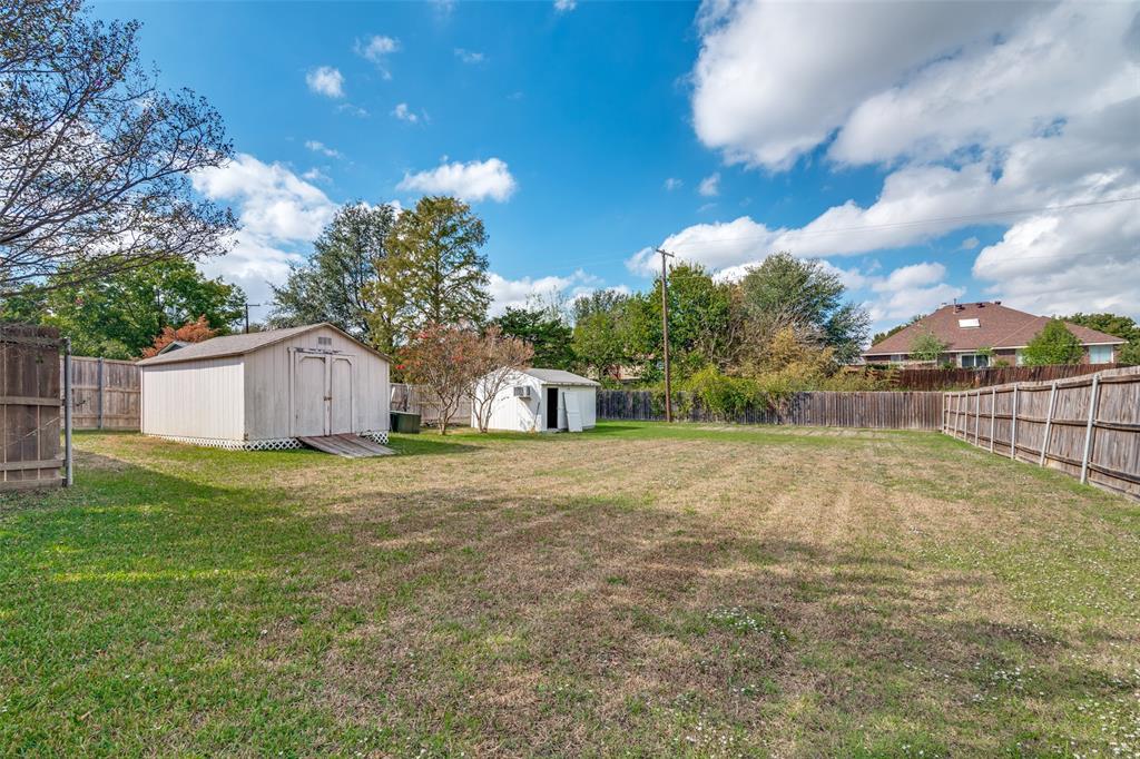 Expansive backyard featuring two detached storage structures and perimeter wood fencing