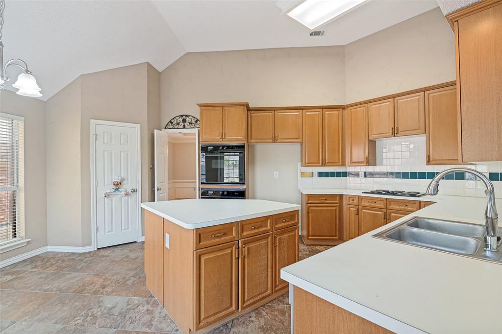 Kitchen featuring wood cabinetry, central island with surface workspace, built-in double oven, gas cooktop, and tile flooring with vaulted ceiling