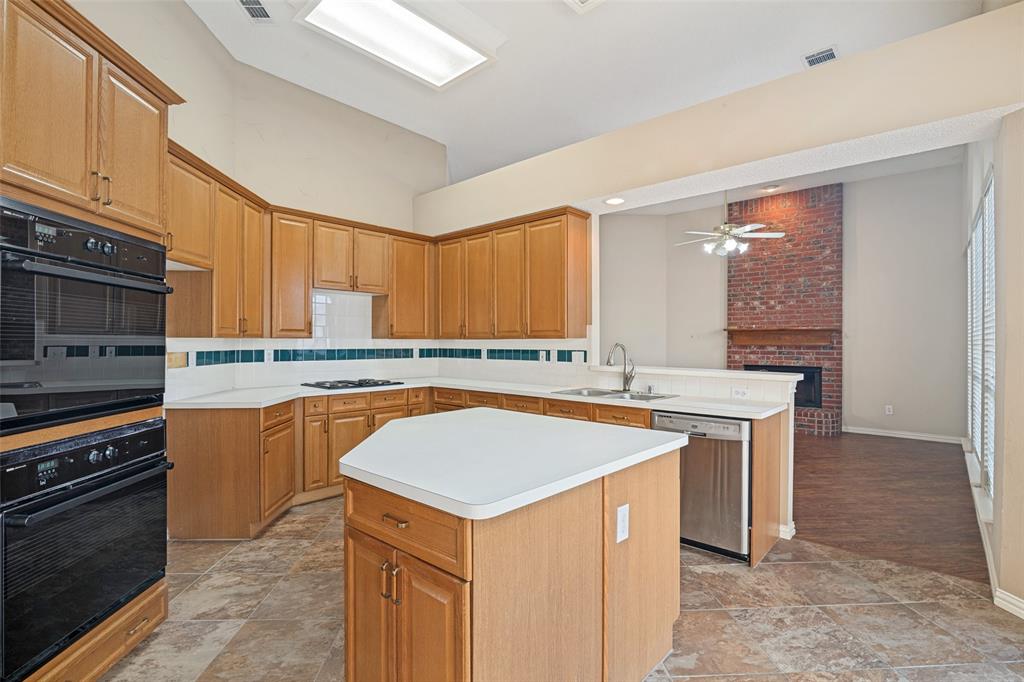 Kitchen featuring wood cabinetry, a central island, built-in double ovens, solid-surface countertops, and tiled flooring