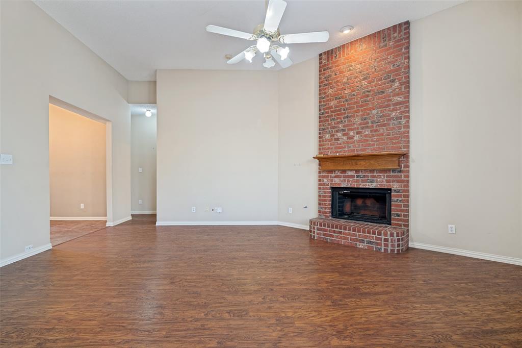 Vaulted ceilings featuring a ceiling fan, wood-finish flooring, and a floor-to-ceiling brick fireplace with a wood mantel Vaulted ceilings featuring a ceiling fan, wood-finish flooring, and a floor-to-ceiling brick fireplace with a wood mantel