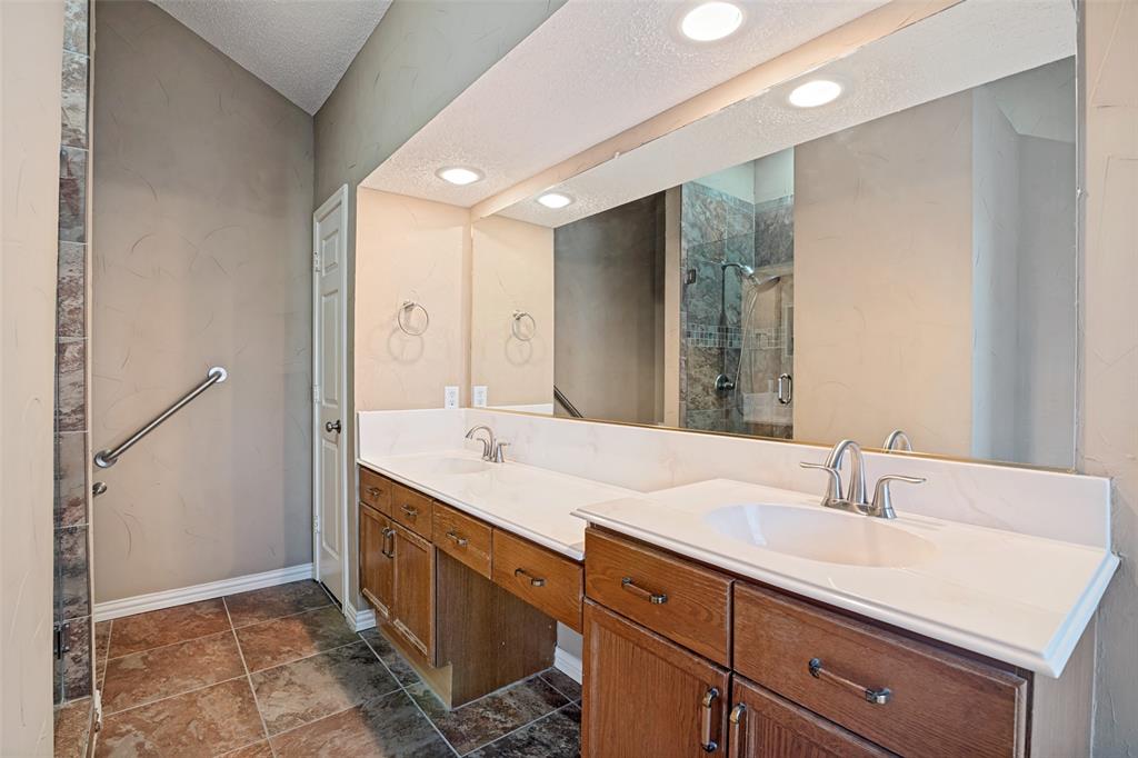Dual-vanity cabinet with white solid-surface countertop and integrated sinks, full-width wall mirror, recessed lighting, and tile flooring