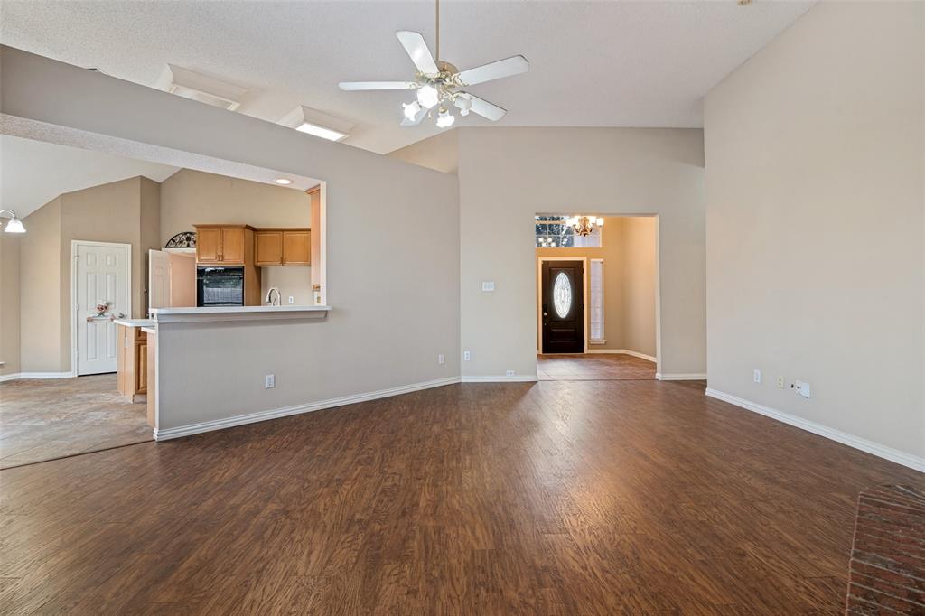 Open concept interior featuring vaulted ceilings, wood-finish flooring, a ceiling fan with integrated lighting, and a breakfast bar