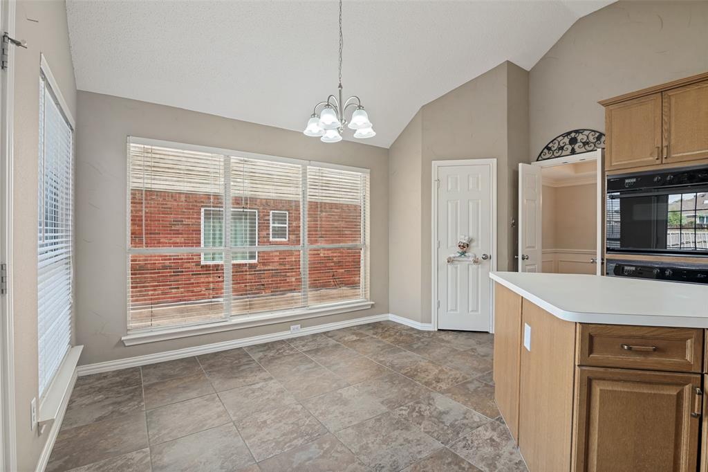 Vaulted ceilings, large picture window with natural light, tile flooring, built-in dual wall oven, and hanging multi-light chandelier