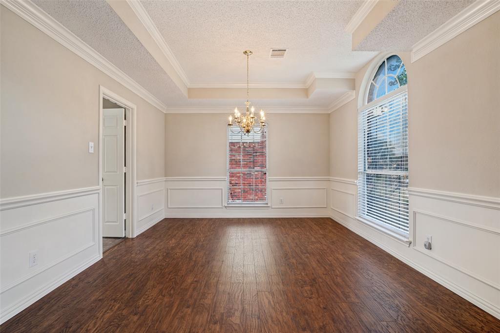 Room featuring wood-finish flooring, wainscoting, a tray ceiling, an arched window, and a chandelier Room featuring wood-finish flooring, wainscoting, a tray ceiling, an arched window, and a chandelier