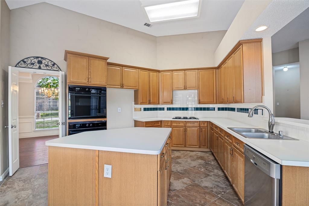 Kitchen featuring vaulted ceilings, wood cabinetry, built-in double oven, center island, and stone-finish tile flooring