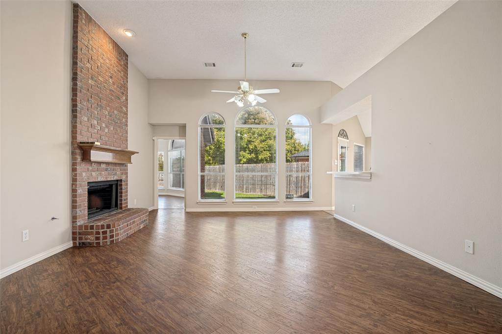High-ceilinged living area featuring wood-finish flooring, a floor-to-ceiling brick fireplace with a wood mantel, and arched windows