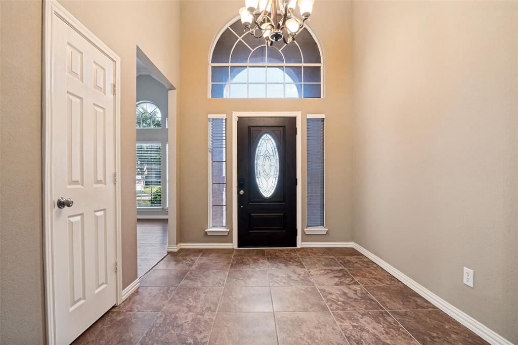 Foyer featuring high ceilings, large-format tile flooring, a multi-paneled door with an oval glass insert, flanking vertical windows, and an arched transom window Foyer featuring high ceilings, large-format tile flooring, a multi-paneled door with an oval glass insert, flanking vertical windows, and an arched transom window