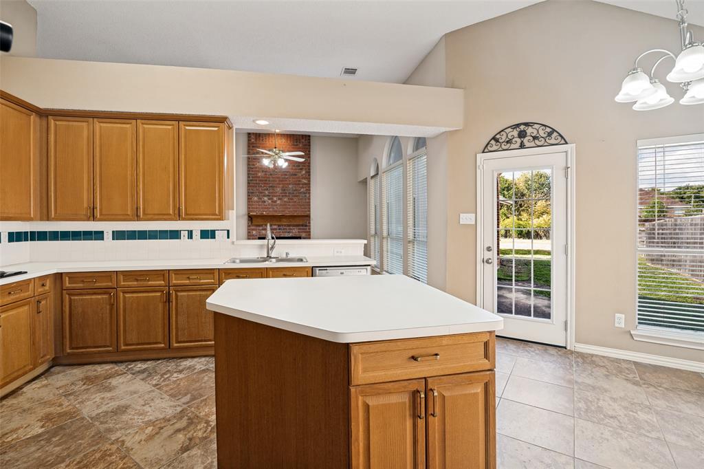 Kitchen featuring wood cabinetry, a central island with a solid surface countertop, a red brick fireplace, tile flooring, and a glass-paneled exterior door with arched decorative ironwork