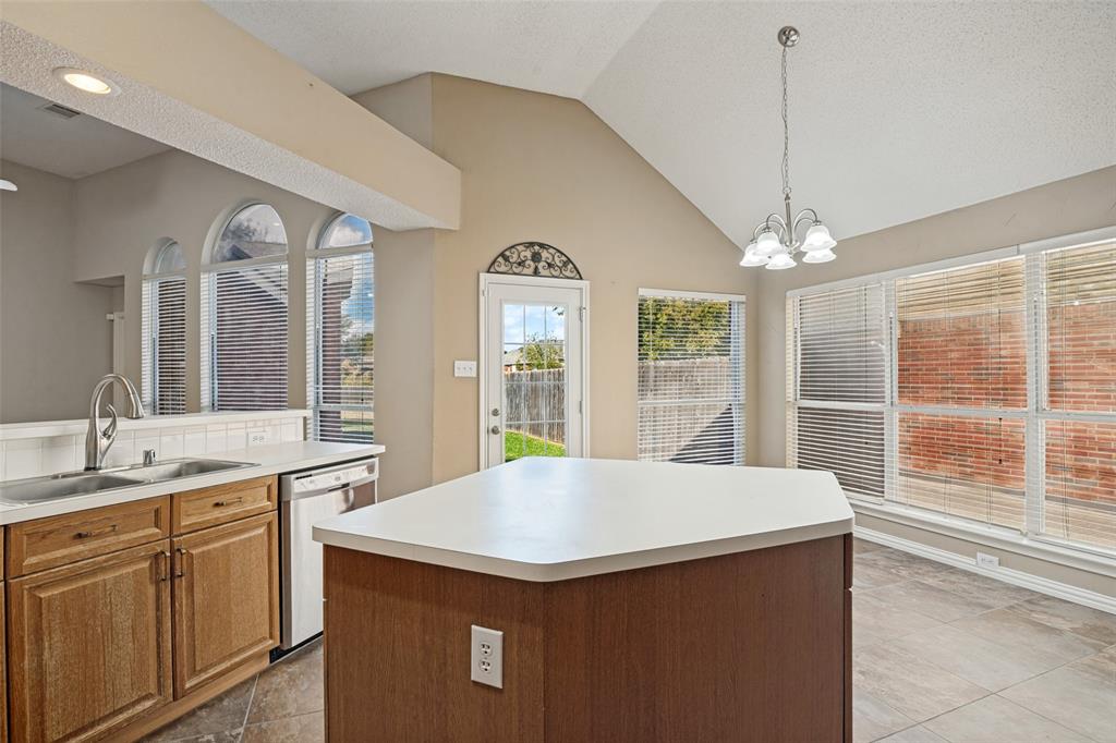 Vaulted ceilings, central kitchen island with countertop seating, large windows with arched accents, neutral tile flooring, and integrated pendant lighting