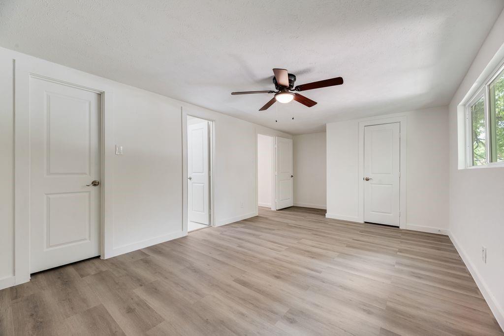 Room featuring wood-finish flooring, white walls, three interior doors, and a ceiling fan with integrated lighting Room featuring wood-finish flooring, white walls, three interior doors, and a ceiling fan with integrated lighting
