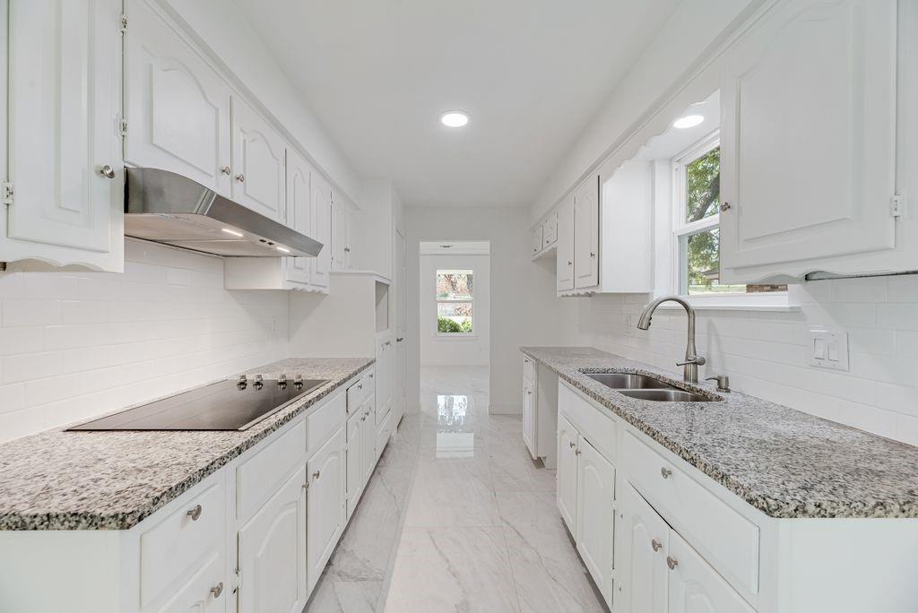 Kitchen featuring white cabinetry, stone countertops, a stainless steel range hood, an electric cooktop, and a dual-basin undermount sink with a gooseneck faucet
