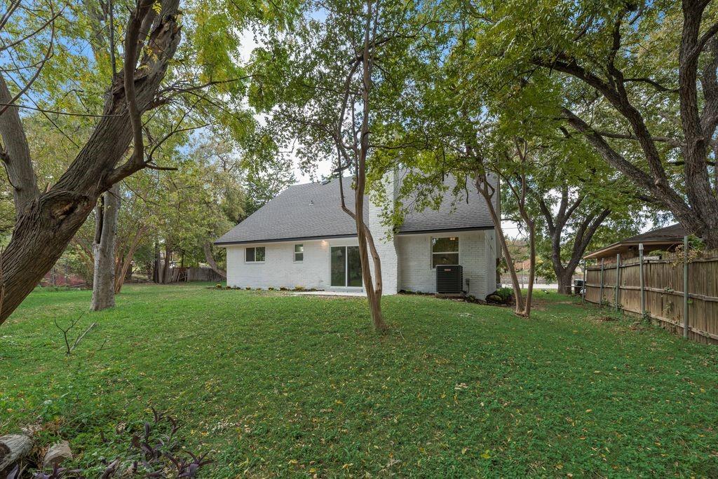 Backyard featuring a painted brick exterior, steep-pitched roofline, mature trees, and a wooden privacy fence