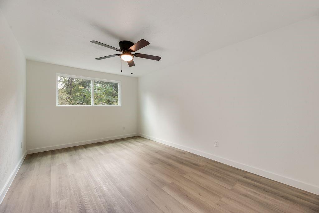 Room featuring wood-finish flooring, a horizontal slider window, and a ceiling fan with integrated lighting