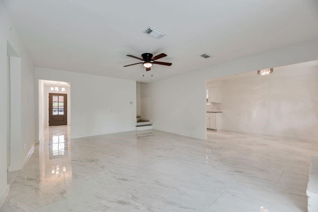 Large living area featuring polished tile flooring, a multi-blade ceiling fan with integrated lighting, and neutral wall tones Large living area featuring polished tile flooring, a multi-blade ceiling fan with integrated lighting, and neutral wall tones