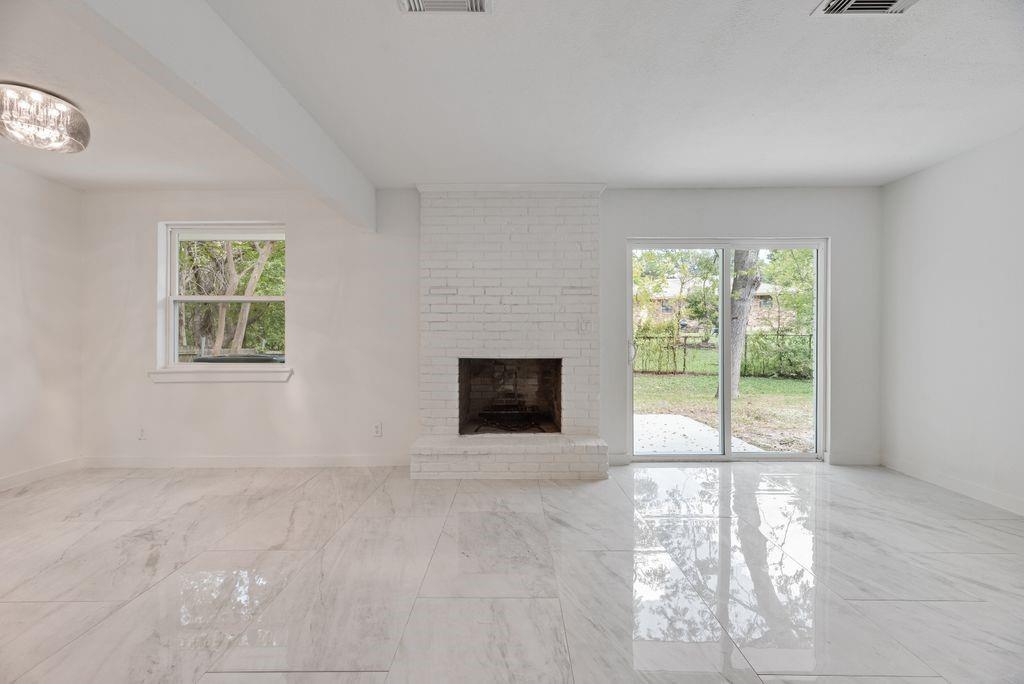 Living space featuring polished stone-finish flooring, white painted brick fireplace, sliding glass door, and flush-mount ceiling lighting